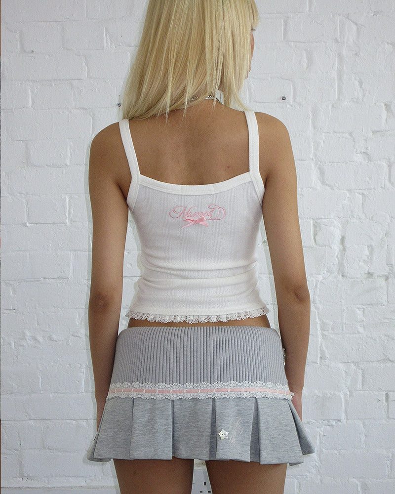 Person with long blonde hair wears NAMED COLLECTIVE® WHISPER PLEATED MINI SKIRT GREY MARL and a white tank top.